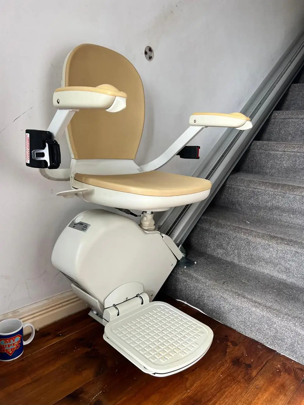 Beige straight stairlift with a folding footrest beside grey stairs in Louth