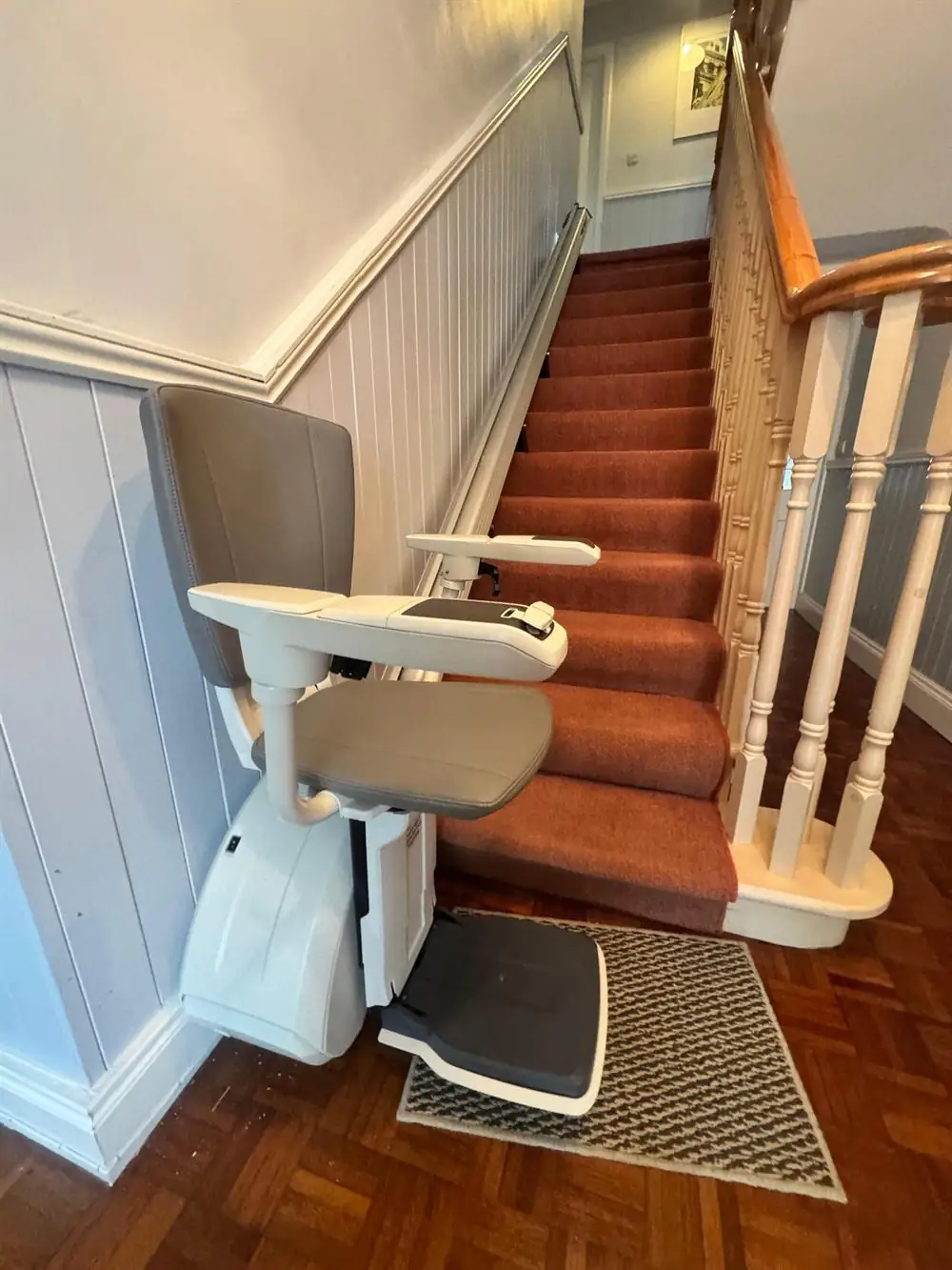 Grey-seat straight stairlift at the foot of a long carpeted staircase in Laois