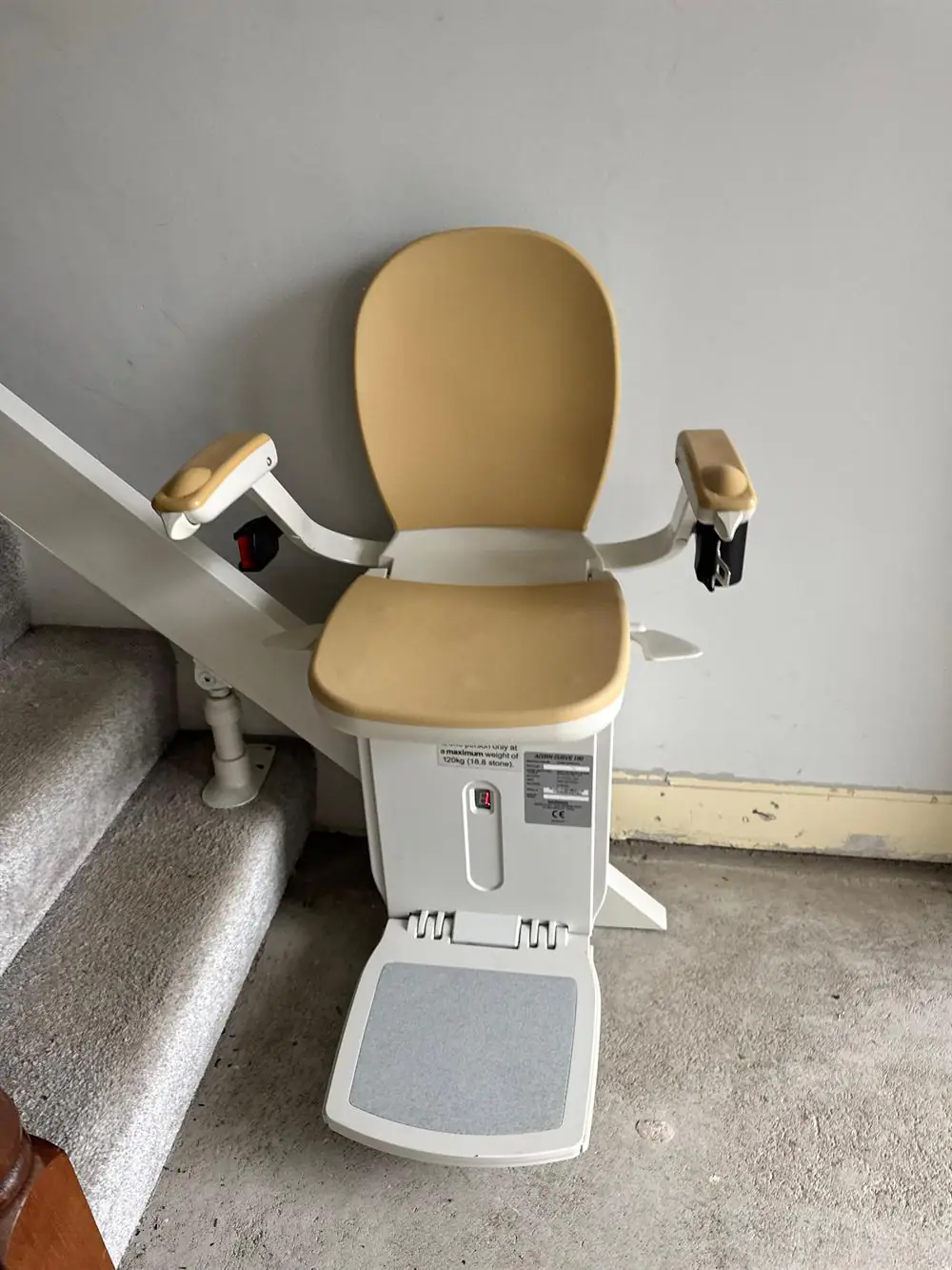 Beige Acorn stairlift installed at the foot of a grey-carpeted staircase in Longford