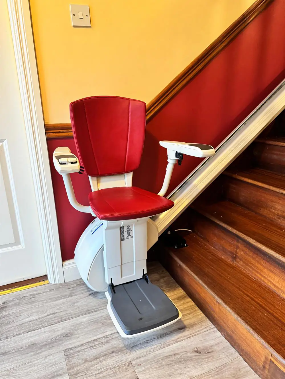 Red upholstered straight stairlift installed beside timber stairs in Clare