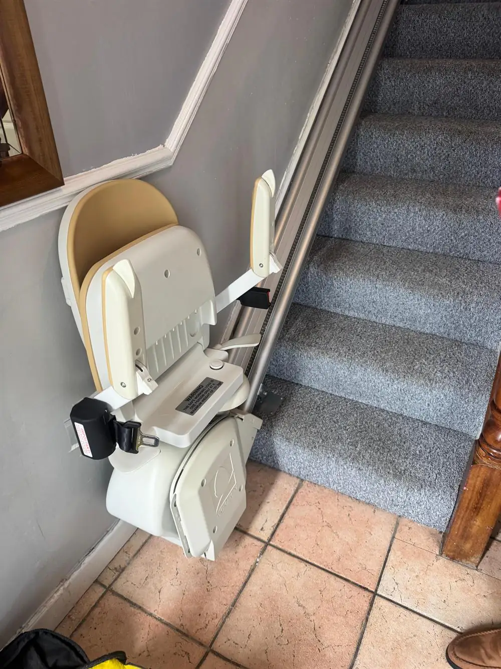 Folded straight stairlift parked at the bottom of grey-carpeted stairs in Donegal