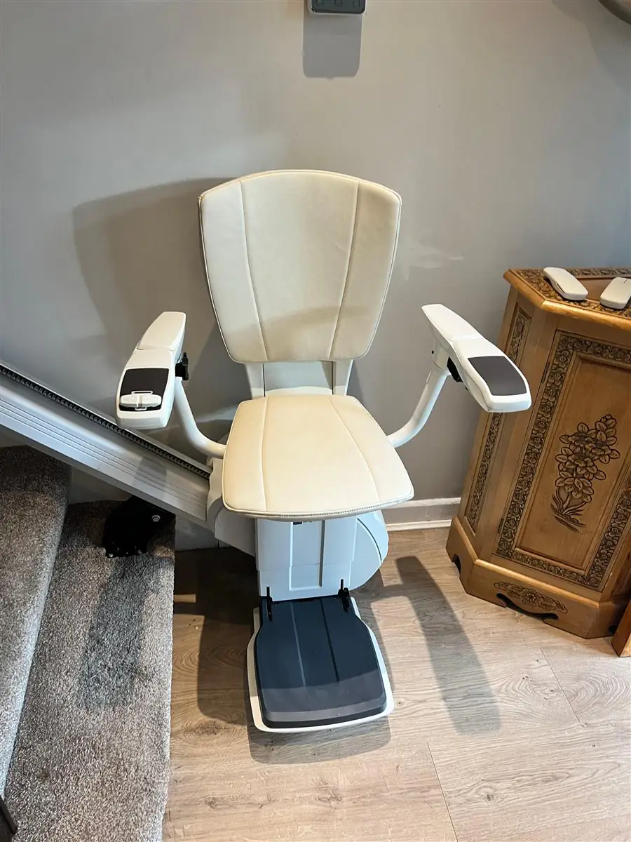 Straight stairlift chair parked at the foot of a carpeted staircase