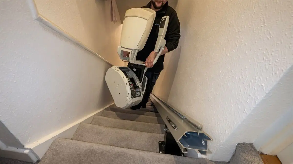 Technician carrying a removed stairlift carriage down a staircase